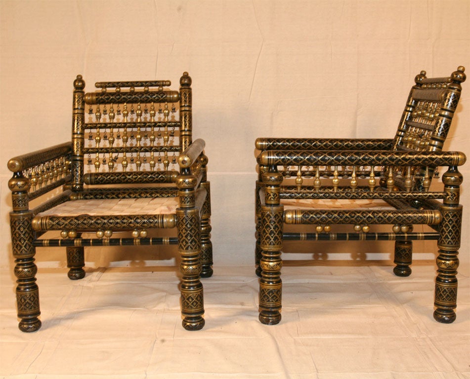 Pair of turn of the century Indian armchairs, ebonized and gold painted and decorated with bells between gold turned spindles. Canvas weave drop-in seats, ready for a cushion.