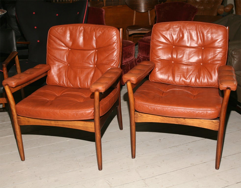 A pair of comfortable wood frame armchairs upholstered in burnt brown tufted leather.

Made by Svenska Mobler.