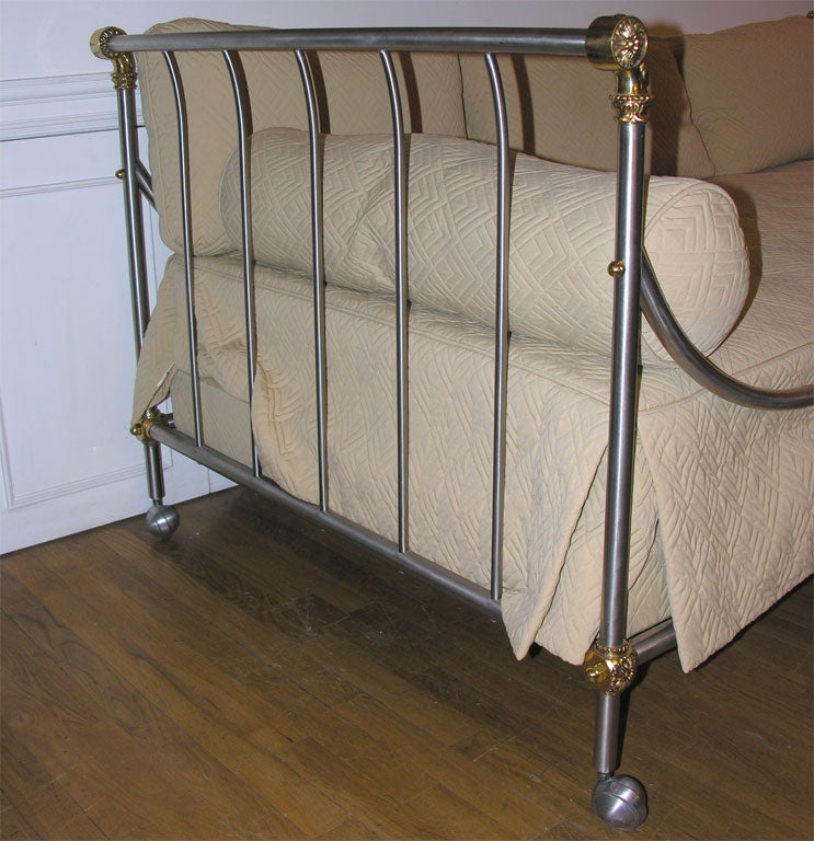 A French Empire style steel and metal daybed, the two ends of equal height having vertical elements supporting upper rail bracketed by bronze elements with rosettes. Design in the manner of Maison Jansen.