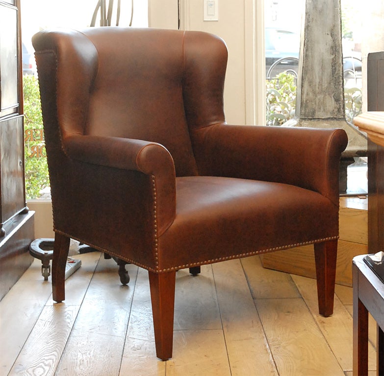 Le fauteuil Halstead de Lee Stanton Editions est un fauteuil à dossier latéral tapissé d'un cuir ambré classique profondément vieilli ou de COM (matériau propre au client). Elle est dotée de clous métalliques ronds et de pieds avant effilés gainés