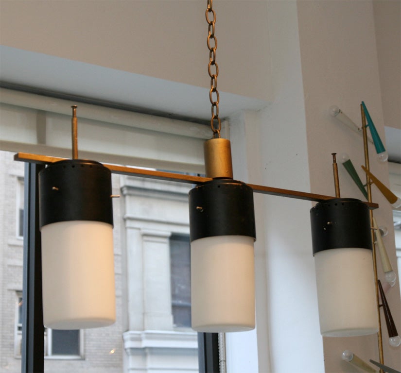 Three-globe ceiling linear ceiling light. Gold metal frame with black metal cups and white cylindrical glass bulbs. The fixture itself is 15.5