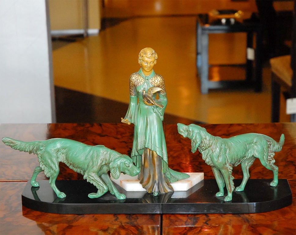 Art Deco bronze statue with green patina depicting woman with two dogs on marble base.