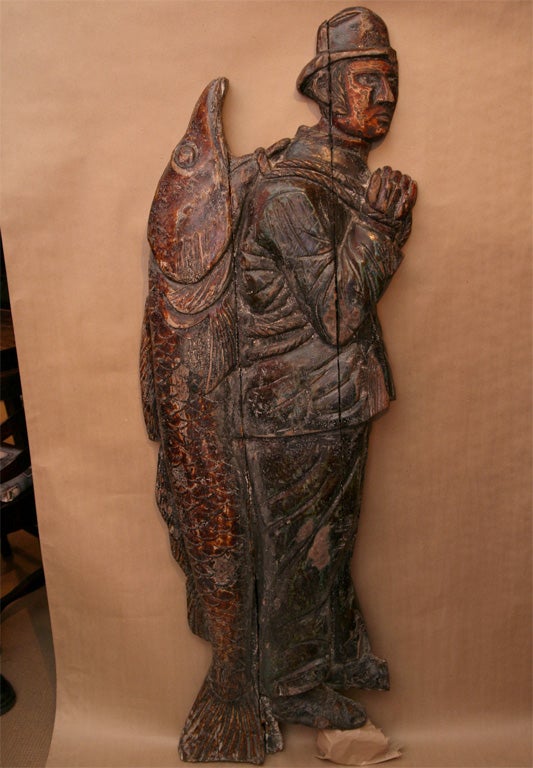 An important wall-mounted English Folk Art trade sign in the form of a nearly life size weathered fisherman wearing his traditional oilskin overalls and jacket with his catch on his back. A fish-oil merchant would have displayed him outside its