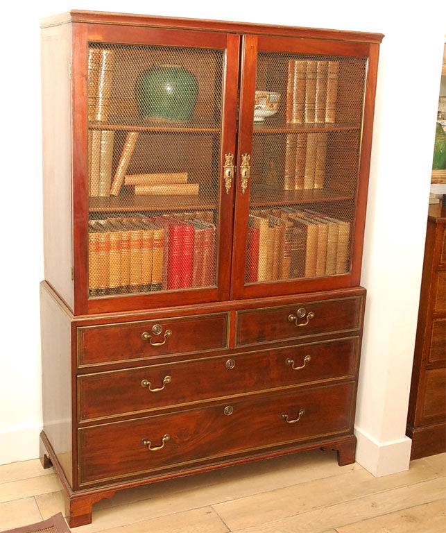 Early 19th century English traditional mahogany bookcase. Serves as a bookcase or display cabinet. Two brass screen door inserts above two short and two long brass inlaid drawers and raised on bracket feet.