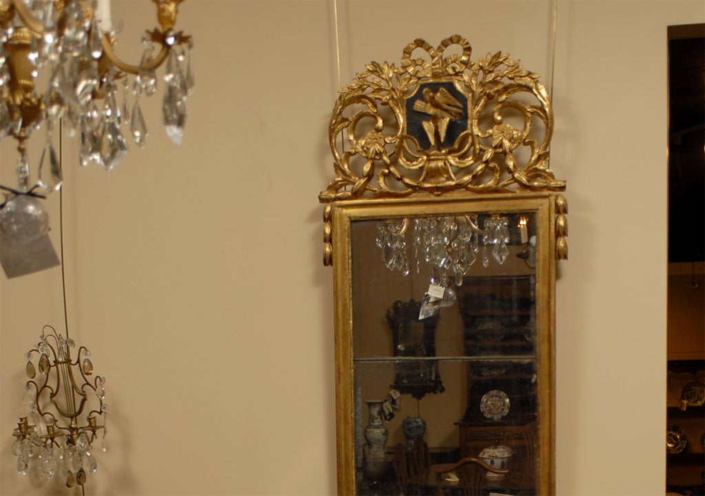 Miroir en bois doré d'époque Louis XVI, surmonté d'une crête détaillée représentant des colombes qui s'embrassent, et flanqué de guirlandes feuillagées le long de chaque côté. La plaque de miroir rectangulaire en deux sections entourée d'une bordure