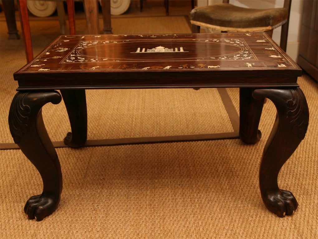 The table's top inlalid with ivory stringing forming a square with inlaid floral motifs in the four corners. Inside the square is ivory stringing forming an elliptical shape which contains a detailed etched ivory image of the Taj Mahal in its