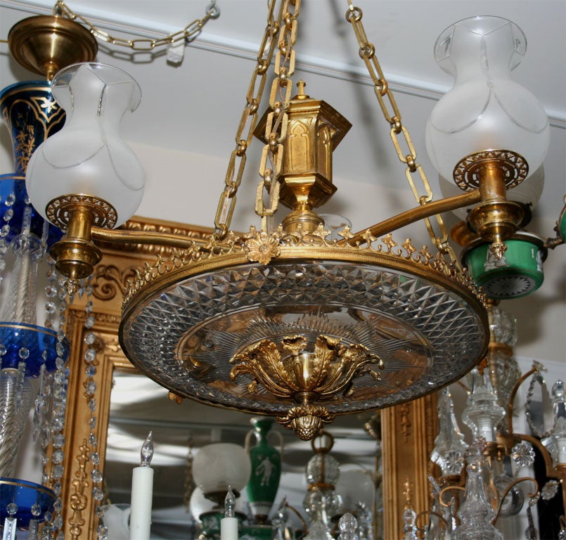An English Regency period gilt bronze chandelier with center ring having trefoil motif framing cut crystal shallow dish secured by plume ornamented finial on underside and having three brass arms with frosted glass shades issuing from Gothic oil