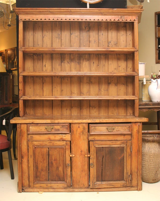 HAVING A MOLDED CORNICE WITH SERPENTINED BRACE BELOW,3 MOLDED  SHELVES, THICK PINE WORK DECK ABOVE 2 MOLDED DRAWERS, 2 PANELLED DOORS BELOW, INTERIOR SHELVES,FLOT BASE.  NOTE: THIS PIECE APPEARS TO HAVE BEEN MADE BY A CARPENTER, NOT A CABINET MAKER..
