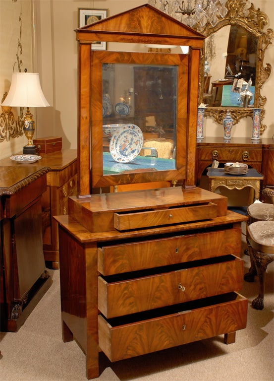 Une inhabituelle commode Empire en acajou avec miroir, datant du premier quart du 19ème siècle et d'origine française.

La pièce en 2 parties : le haut un miroir de coiffeuse avec petit tiroir, le bas une commode.  Le tout en acajou figuré.