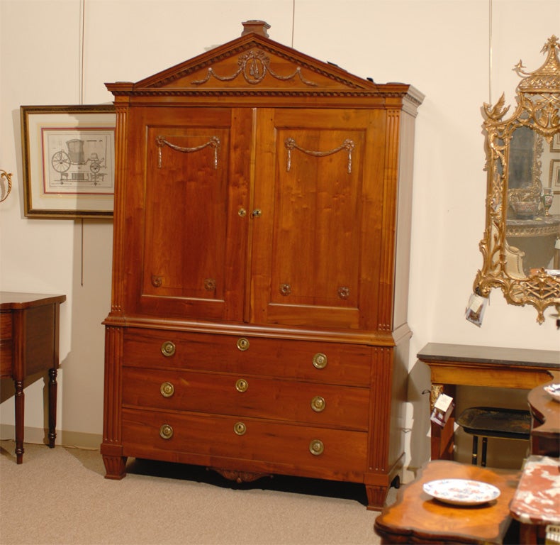 A large fruitwood Linen Press/Cabinet in the neoclassical taste with fluting and laurel leaf swag design, originating during the turn of the 19th century.