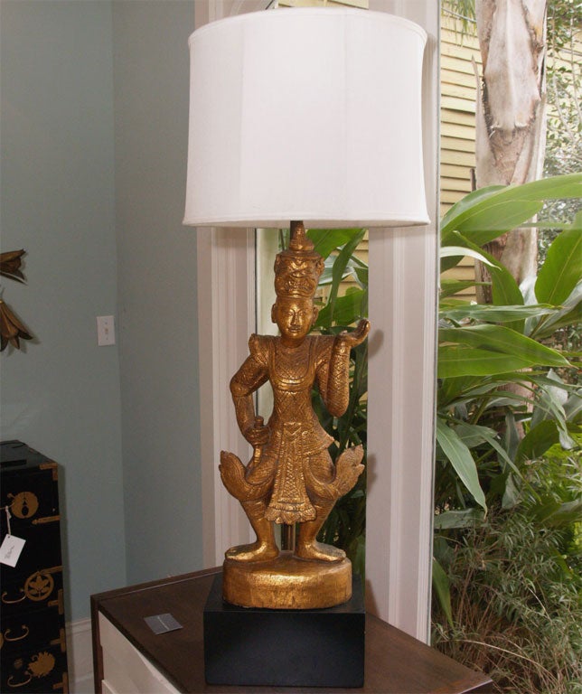 Attractive two-light table lamp in gilt over plaster; the form suggesting a Thai nobleman; black-painted plinth; two decorative pull chains; shade not included.