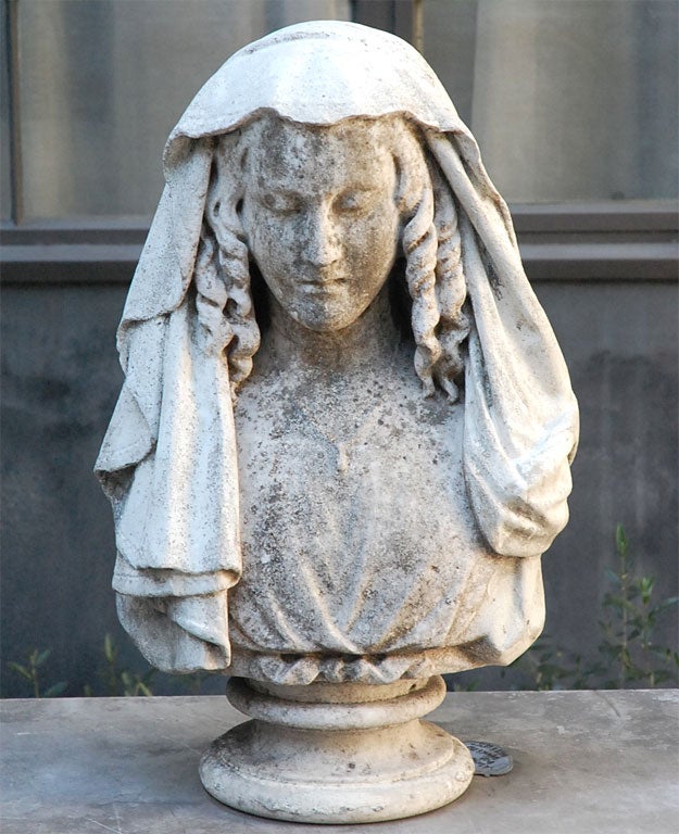 A bust in stone of a serene woman in elegant drapery on a pedestal base.