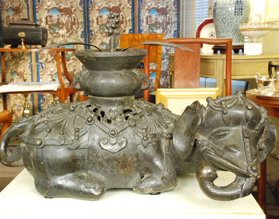 Beautifully patined incense burner in the form of a reclining elephant.  The plant at the top is a lid.  There are reticulations below the urn for escaping smoke.