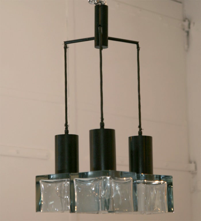 Three thick blue glass cubes suspend black from black metal arms.