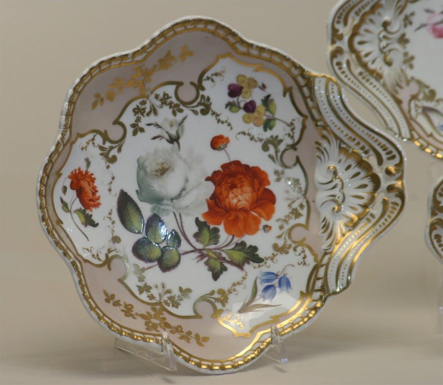 Set of four early 19th century Spode felspar porcelain plates. The hand painted botanical decoration with vibrant naturalistic colors is off-set by the pale embellished border with gold trim on a shell shape. One set measures 8.5