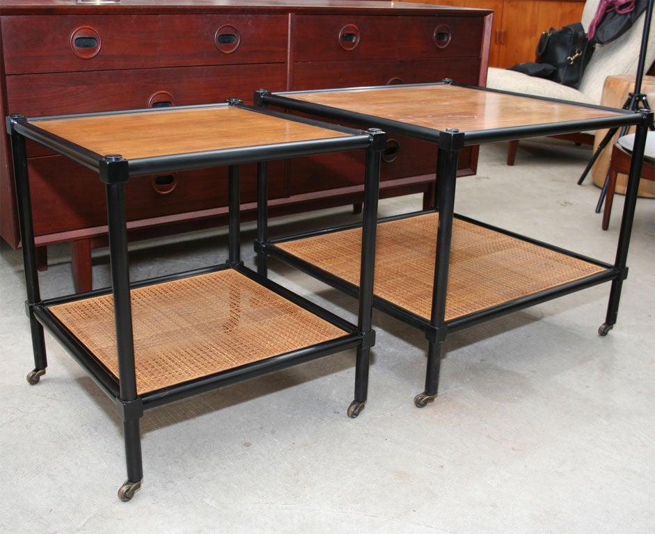 2 Baker side tables on castors with ebonized frames and cane and walnut shelves.  One table is larger than the other.  The smaller of the 2 is 20