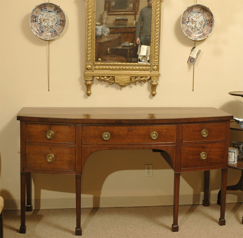 A George III period Sideboard in rich Mahogany, with Bow-front design, inlaid borders, and ample compartments for storage. Dating from the fourth quarter of the 1700s and originating in England.<br />
<br />
The body composed of four sliding