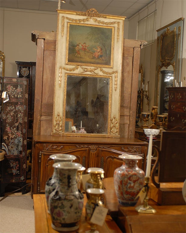 Un grand miroir Trumeau d'époque Louis XVI, avec un cadre peint en crème et doré présentant des motifs néoclassiques en relief, et avec une scène supérieure à l'huile sur toile représentant des enfants jouant dans une forêt. 

Le miroir date du