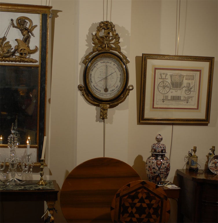 Crested double-headed eagle atop an oval giltwood and painted black frame with neoclassical borders and carved designs. 

The dial with metal arms and exposed thermometer coil, and featuring various barometric conditions and temperatures in