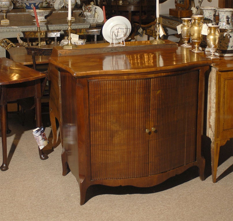 A Tambour-fronted Buffet in Mahogany, featuring a serpentine form on the front and sides, raised atop cabriole feet with shaped apron. Dating from the first quarter of the 1800s, and English in origin.

The body with graceful curves throughout,