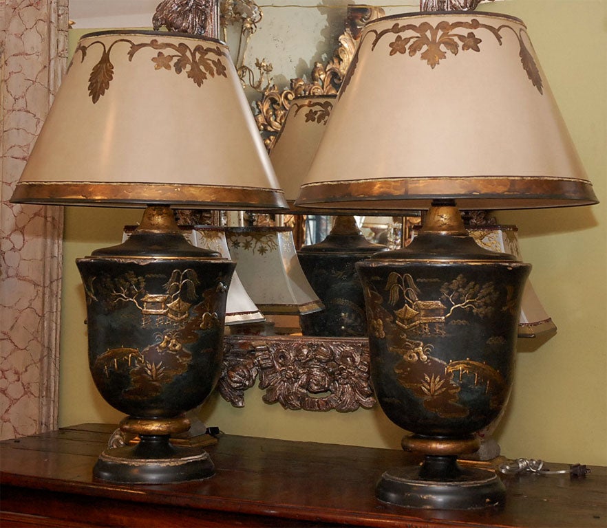 A handsome pair of hand painted and lacquered chinoiserie lamps with custom painted parchment shades.  The bases have charming delicate scenes of trees, bridges, village houses in raised gold and silver relief on a black lacqued backround.  The
