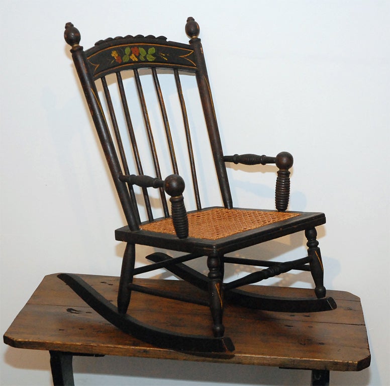 WONDERFUL 19THC ORIGINAL BLACK PAINTED AND DECORATED CANE SEAT CHILD'S ROCKING CHAIR IN GREAT CONDITION. THIS BEAUTY COMES FROM PENNSYLVANIA AND HAS HAND PAINTED FLOWERS ON THE TOP CROWN OF THE ROCKER AND THE ORIGINAL CANE SEAT. THIS ROCKING CHAIR