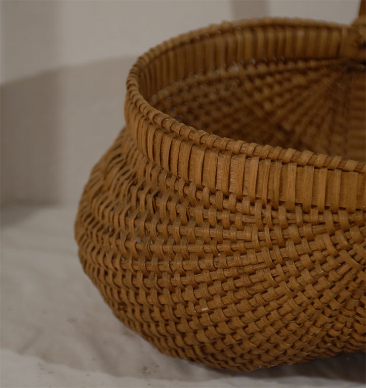 A large and well-executed split oak fanny basket in excellent condition.  Very nicely woven; very tight; well proportioned handle.  At some point, someone put a matte varnish on the basket, but it has oxidized nicely.