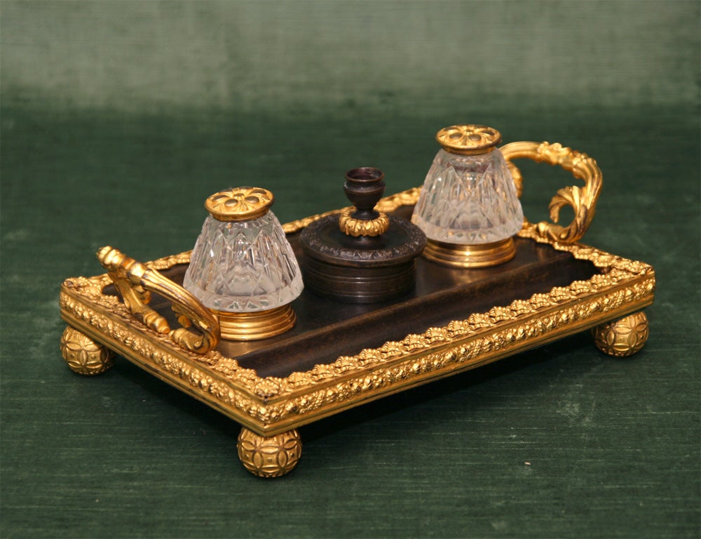 Fine Regency Period Bronze and Gilt Bronze Ink Stand; With Two Cut-Glass and Bronze-Lidded Ink Bottles Flanking a Center Receptacle with Candle Holder Lid; Raised on Exquisitely Detailed Bronze Ball Feet, England, c. 1825<br />
<br />
12 inches