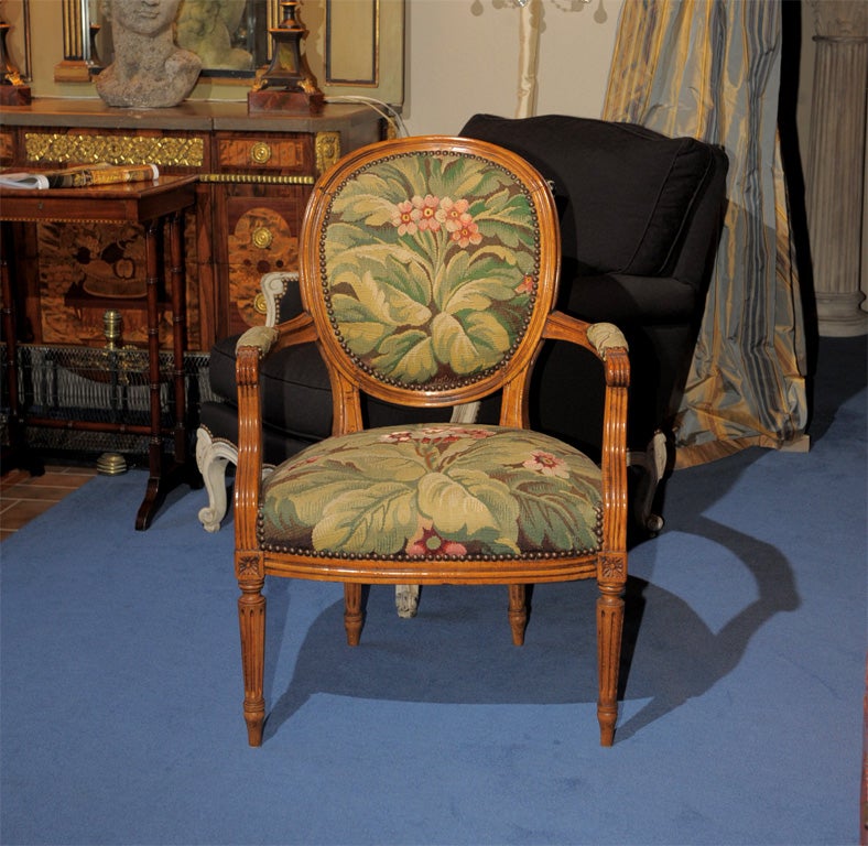 The circular molded back continuing to padded arms over  fitted seat raised on tapering fluted legs, overall upholstered in tapestry predominately greens with red, depicting voluminous leaves and foliage, back covered in coordinatine plaid.