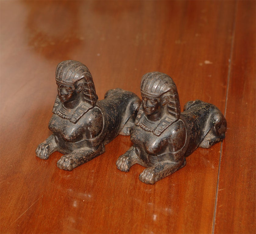 A small pair of iron sphinx statues in the Greek Mythology style, i.e. the head and breasts of a woman and the body of a lion.