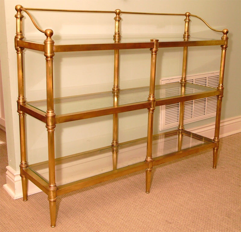 Three-tier etagere in satin brass with upper gallery rail; shelves in glass; finely detailed turnings and joinery throughout