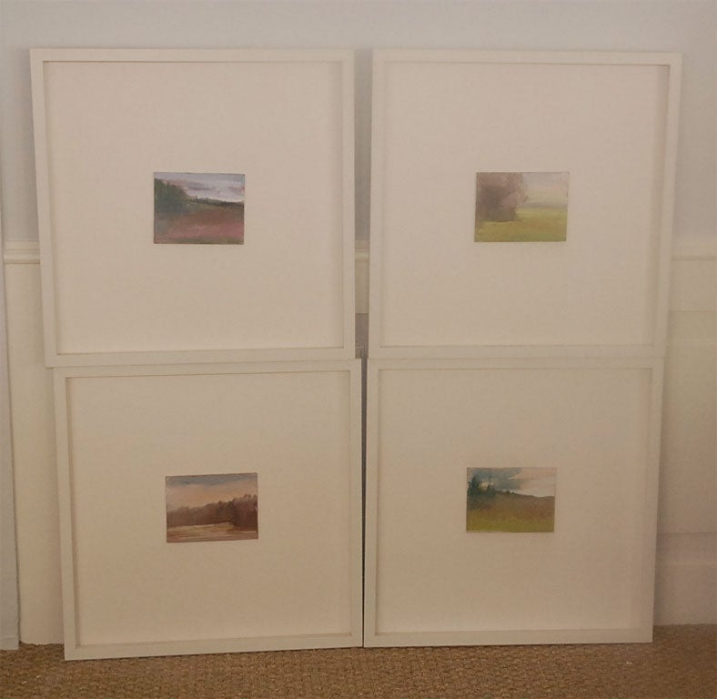 A set of four petite paintings depicting lush landscapes in tones of browns, pinks, and blues by Susan Amato. Newly framed in large matte white frames.