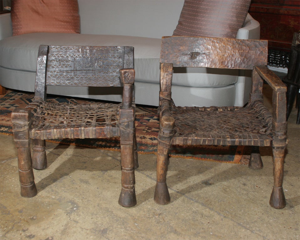 One-armed Ethiopian chairs with webbed seats of leather strips. Rustic. Unique style and design of legs, structure and seat.  Only chair on left still available. Dim: 20.5