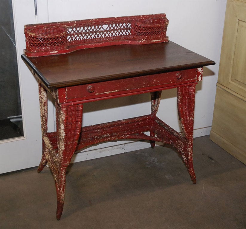 Wicker desk with oak writing surface over a full length drawer. The wicker and wood surmount has end compartments to position useful items. The desk stands on four splayed legs, has a lower skirting and other support features which are also wicker 