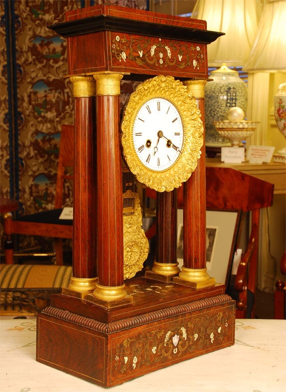 Pendule de style portique en tulipier français avec incrustations fines de style Boulle en nacre et bronze. Mouvement français de huit jours avec une pendule en fer forgé et en bronze doré. Quatre colonnes de soutien avec chapiteau, bases et cordons