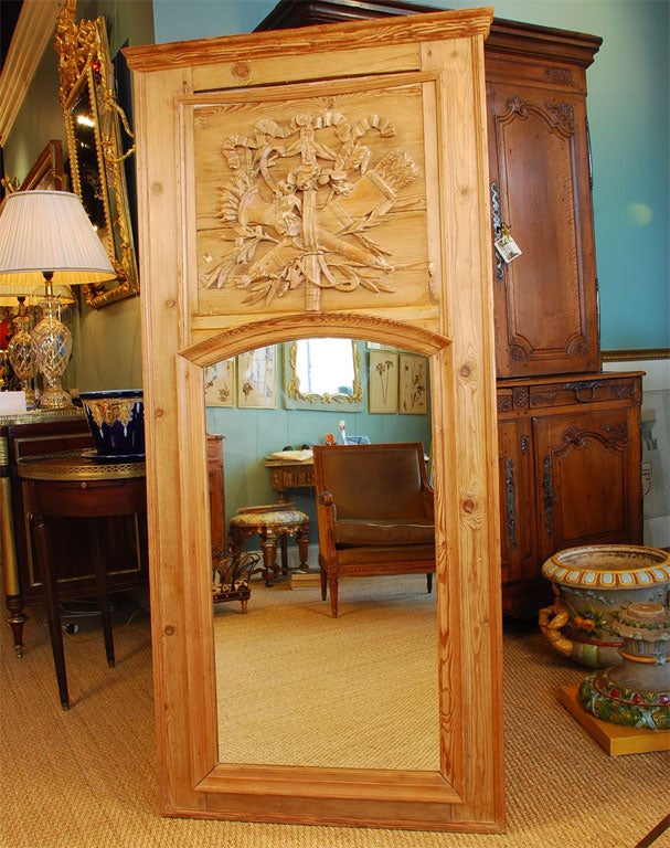 Louis XVI period trumeau mirror in carved pine. The original paint has been stripped, and the wood has been waxed. The neoclassical carving features a torchère and fasces, ribbon and laurel leaves. The glass appears to be more recent.
