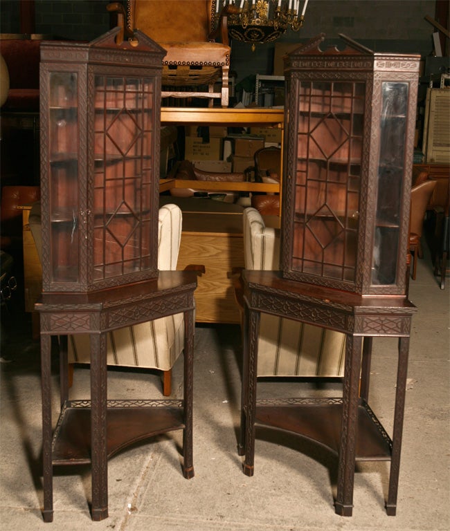 Pair of Edwardian corner display cabinets, in mahogany,  for silver, glass or curios, in the Chippendale style, with astregal glass doors, broken pediment tops, on stands edged with fretwork.  The depth from back corner to front of stand measures