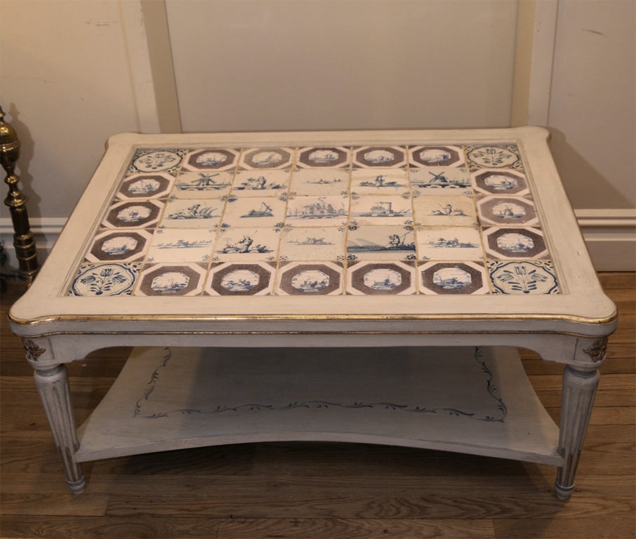 A custom made Swedish Gustavian style two-tiered coffee table with round and tapered stop fluted legs joined by stretcher. The lower surface having concave shaped side and hand painted decoration.  The upper section with 18th c. Delft tile top. The