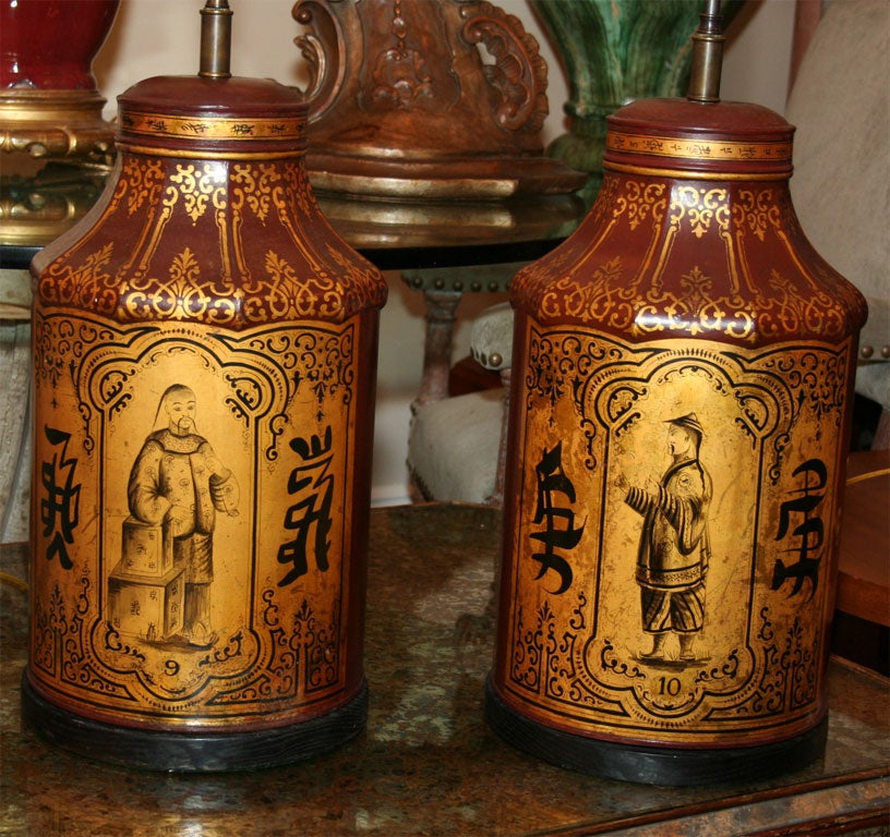 A pair of octagonal English tole tea canisters with hand painted and stenciled decoration on a red ground with gilt reserve, the center panel having a Chinese figure on a gilt ground with Chinese calligraphy now mounted as lamps on a turned ebonized