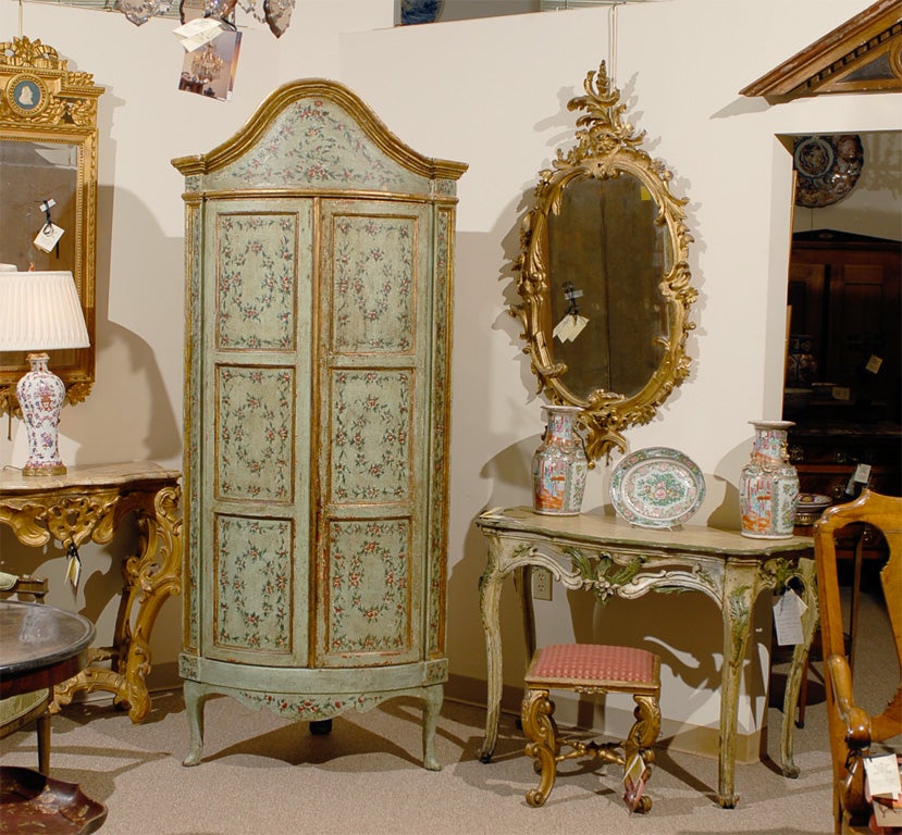 An 18th century Venetian Bowfront Corner Cabinet decorated in pale green ground with floral and parcel gilt decoration, dating from the second half of the 18th century and Italian in origin.<br />
<br />
The exaggerated bonnet top is over two