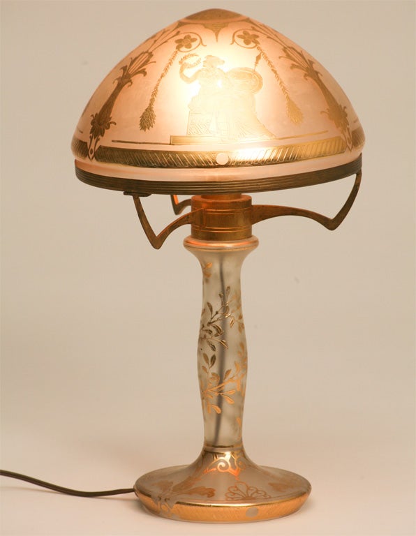 A lovely handblown two-part table lamp with acid etched and gilded decoration depicting Romanesque figures. The matching dome shade rests in the gilded fitter rim. This is a very decorative and functional piece, pretty unlit or lit up and ready for