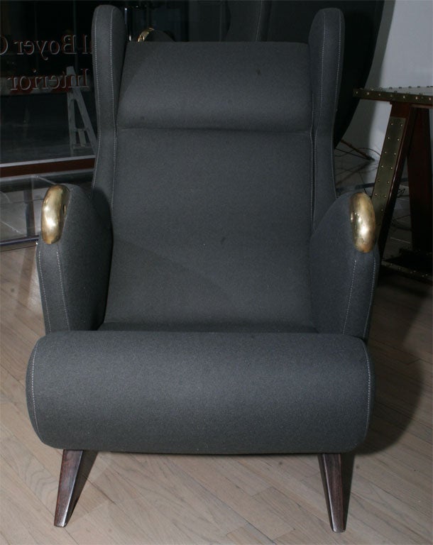 A large pair of wing chairs by Erton, nicknamed Cadillac upholstered in a charcoal wool with brass arm tips. Very comfortable.
