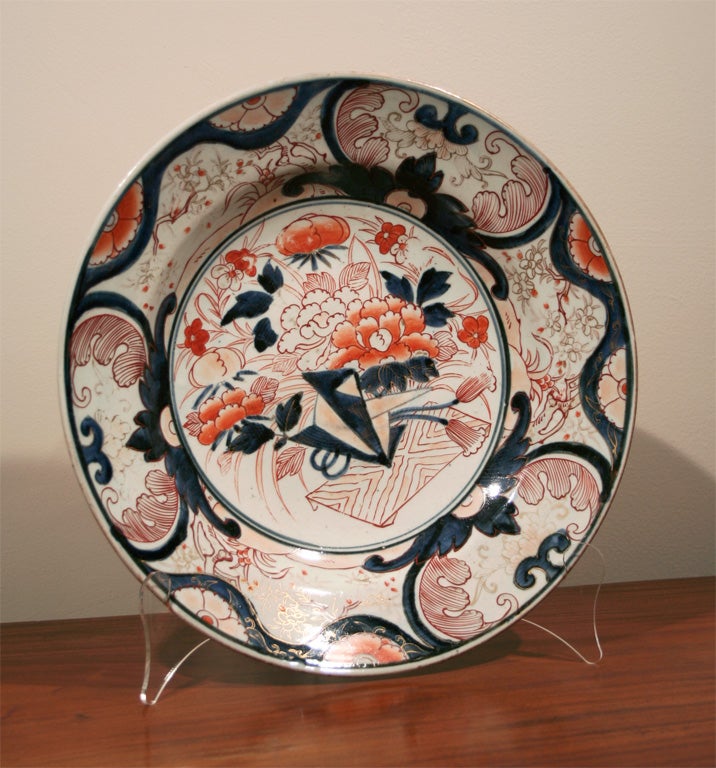 Chinese Imari low bowl under an over-glaze decoration.  Center depicting base on platform with mixed flowers. Outer circle with trees and subtle diapering, over-painted with lattice in blues, bricks, and gild.