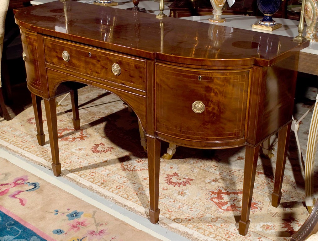 Handsome George III mahogany bow front sideboard, beautiful beveled top, with an unique brass plate rail, over a conforming case fitted by a centralized drawer flanked to either side of cupboard doors, overall with delicate satinwood stringing,