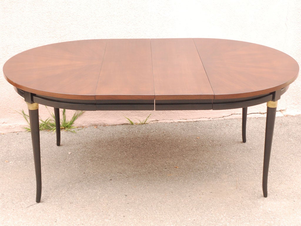 Beautifully restored round Baker dining table with walnut top and black legs with brass accents. With 2 leaves it becomes an oval.