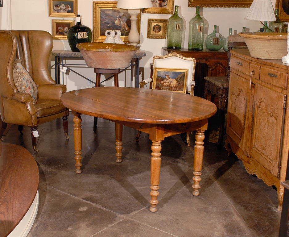 A French walnut oval drop leaf table from the late 19th century with removable top.  This French oval drop leaf walnut farm table circa 1870 features an oval removable top over a rectangular belt with a drawer resting on four turned-wood and