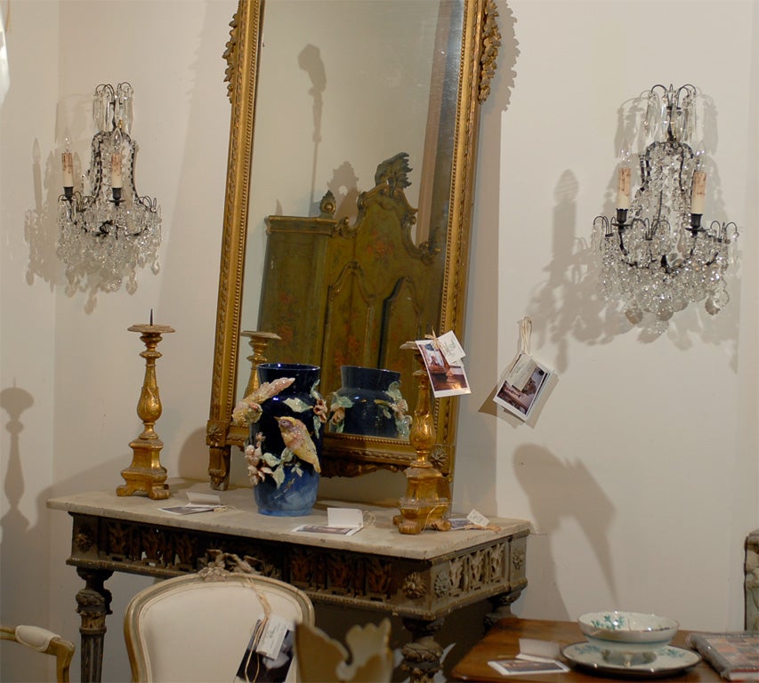 A pair of French Rococo style crystal two-light wall appliques from the late 19th century with metal armatures and faceted crystals. Born in the later years of the 19th century, each of this pair of French Rococo style wall sconces features a dark