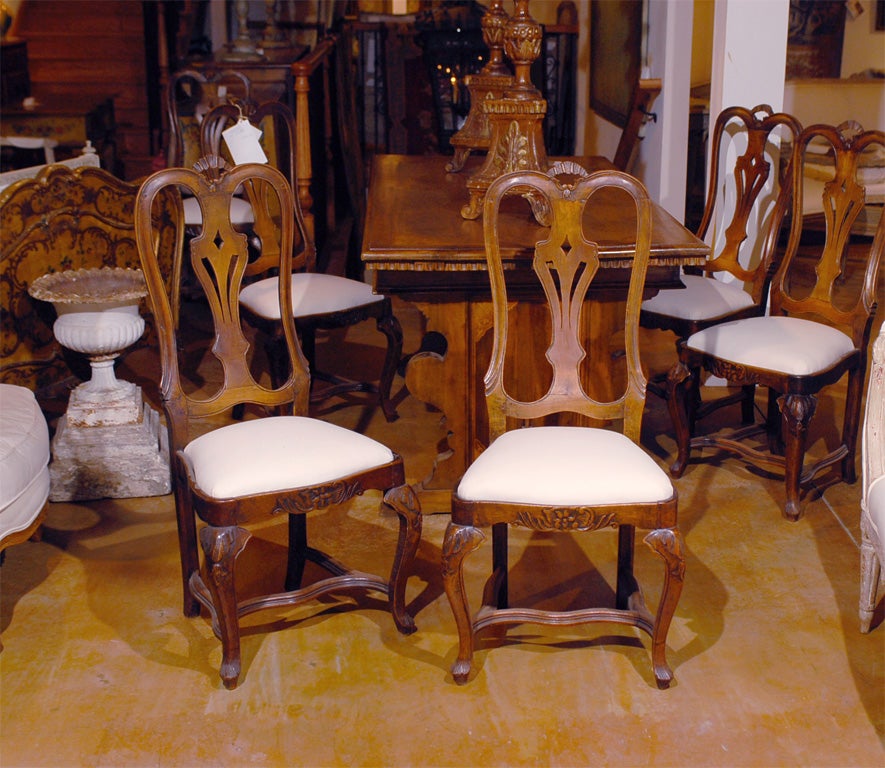 A set of six Danish Rococo style early 19th century walnut dining chairs with carved splats, upholstered seats and cross stretchers. Each of this set of six Rococo style dining chairs features a carved crest resting on a tall, slightly slanted