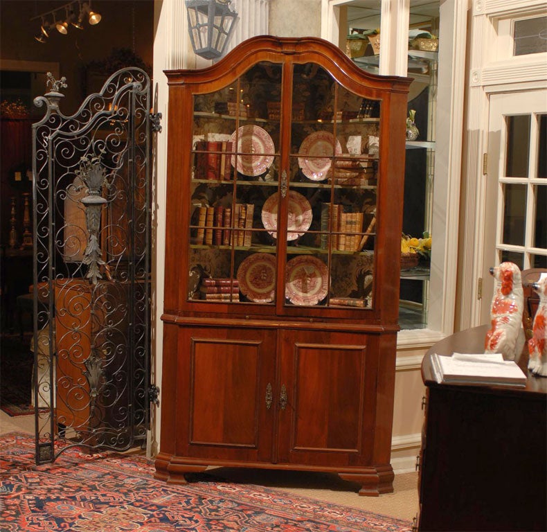 Rare 18th century Dutch corner cupboard of mahogany with glass doors, beveled edges, canted corners, and bracket feet. 19th century chinoiserie fabric lines the interior which has three shaped, painted shelves in the top of the cupboard and one