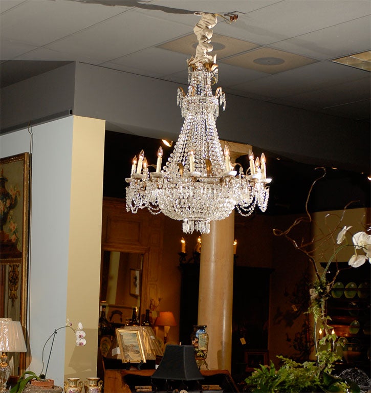 This exceptional crystal chandelier is French in the Empire style, circa 1900.  It has gold leaves in tole with twelve graceful iron arms.  There are three tiers of cut crystals reflecting light off each other.  This formal example of French crystal
